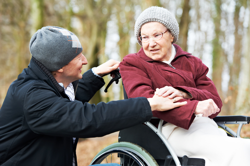 Older man crouching to talk with older woman in wheelchair Older man crouching to talk with older woman in wheelchair